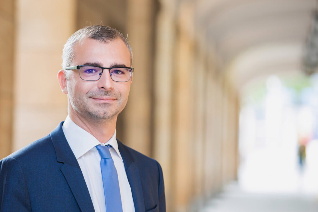 Businessfotos in Dresden von einem Herren in Anzug. Das Foto wurde draußen aufgenommen und hat einen modernen Hintergrund. Perfekte Businessfotos außerhalb der normalen Fotos im Studio.