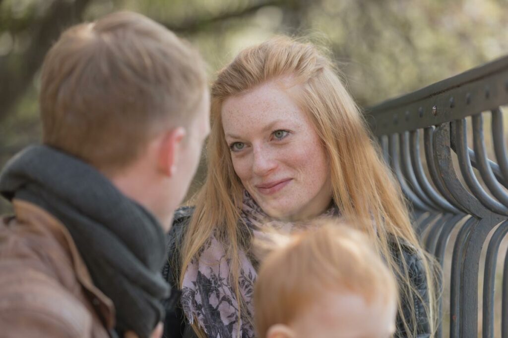eine junge familie sitzt auf einer parkbank in dresden, dabei schaut die frau ihren freund verliebt an und lächelt dabei. aufgenommen ist dieses foto im frühling in dresden in einem park