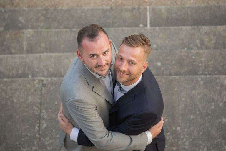 ein gleichgeschlechtliches Ehepaar steht nebeneinander und schauen in die Kamera der Hochzeitsfotografen Möbeln
