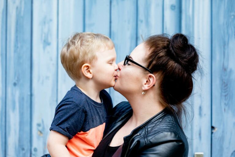 ein junge küsst seine mama, die mama hat den jungen auf dem arm und sie genießt die zeit zu zweit - Erinnerungen für die Ewigkeit. Bilder die außerhalb eines Fotostudios angefertigt werden - natürlich und authentisch