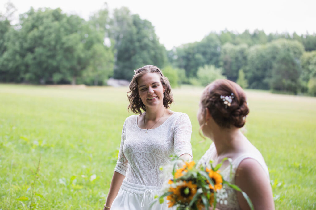 zwei Frauen gehen auf einer Wiese entlang, halten sich an den Händen und schauen sich verliebt und glücklich an zu ihrem Hochzeitstag in Bautzen